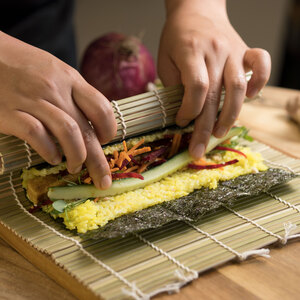 two hands in the process of rolling sushi on a sushi rolling mat