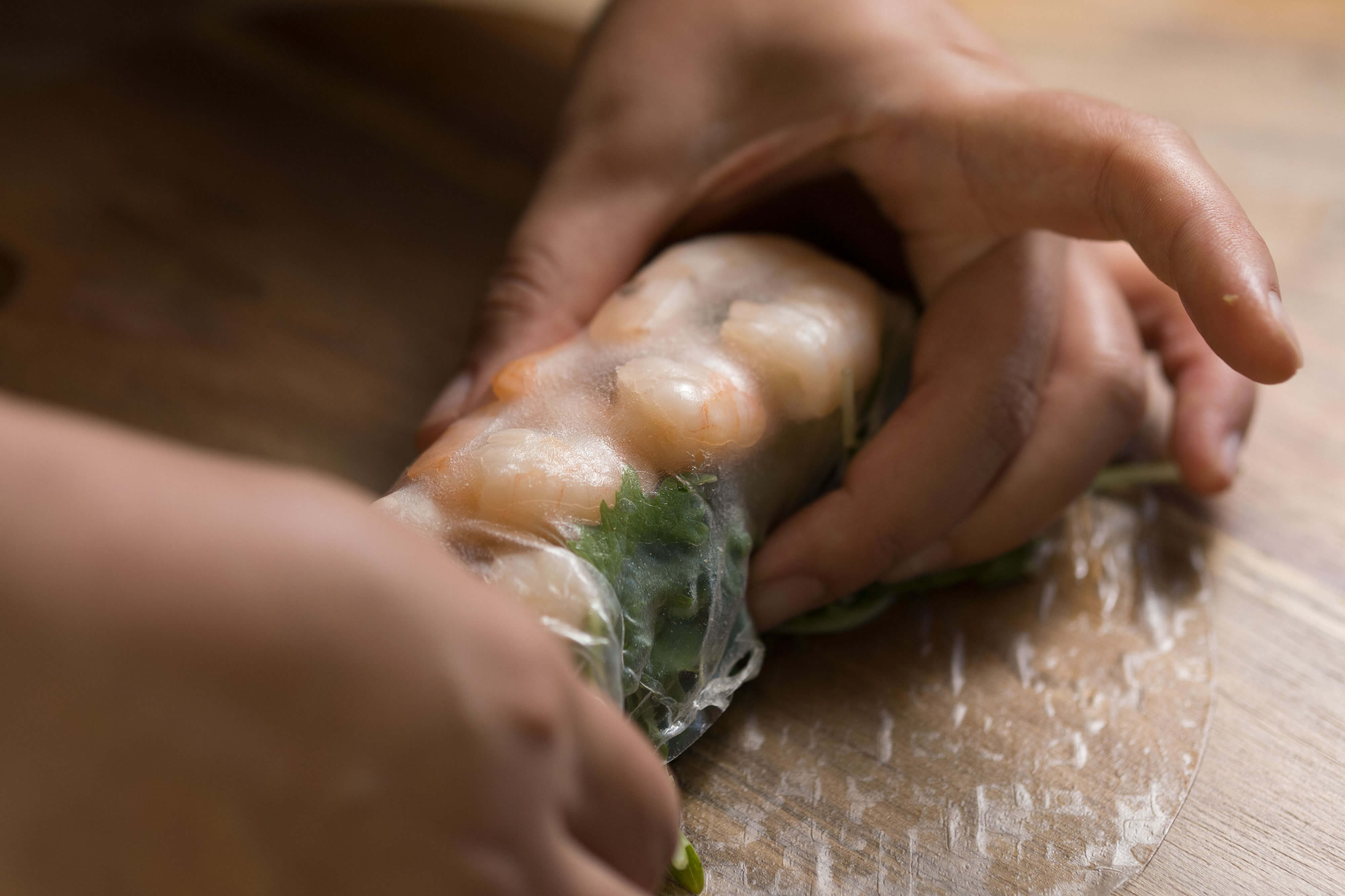 Hands folding a rice paper roll with shrimp and green vegetables