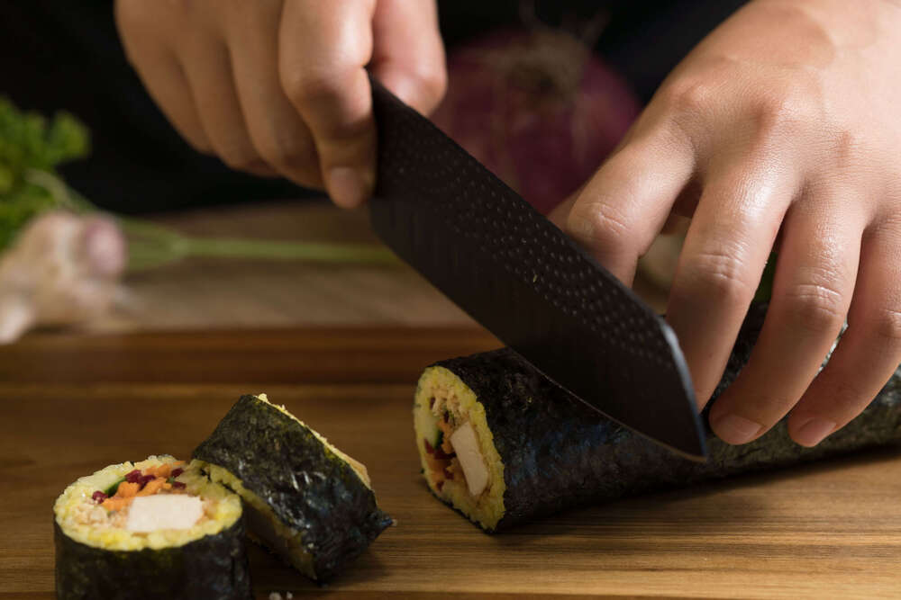 Hand and black knife cutting through a roll of sushi